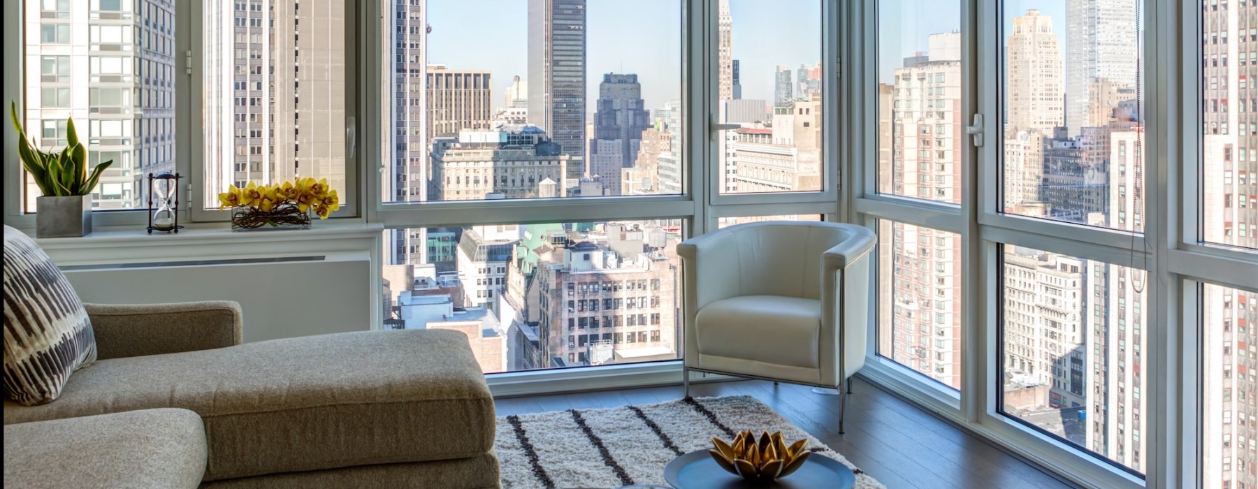 living room with a chair and two walls of window overlooking a city